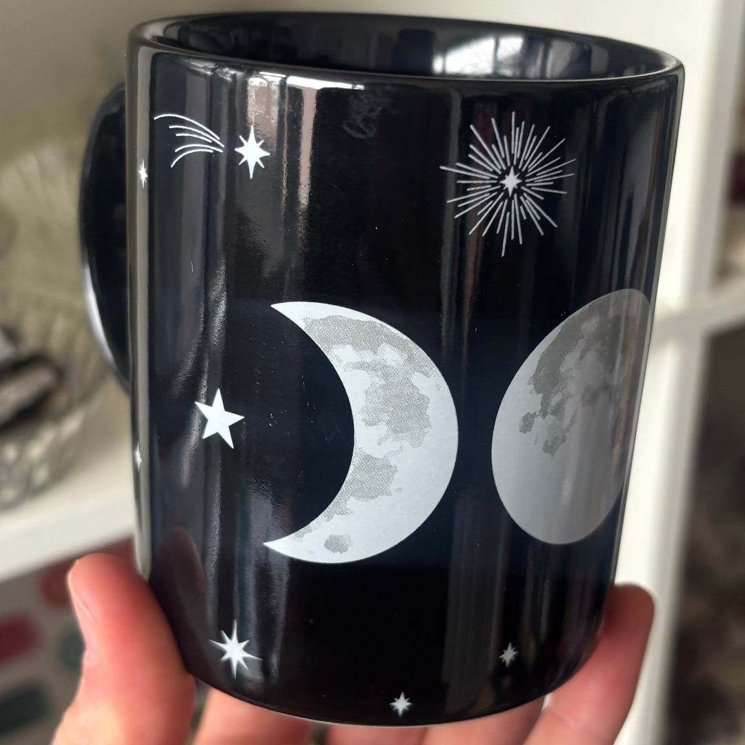 Black mug with moon and star design held by a hand against a blurred indoor background