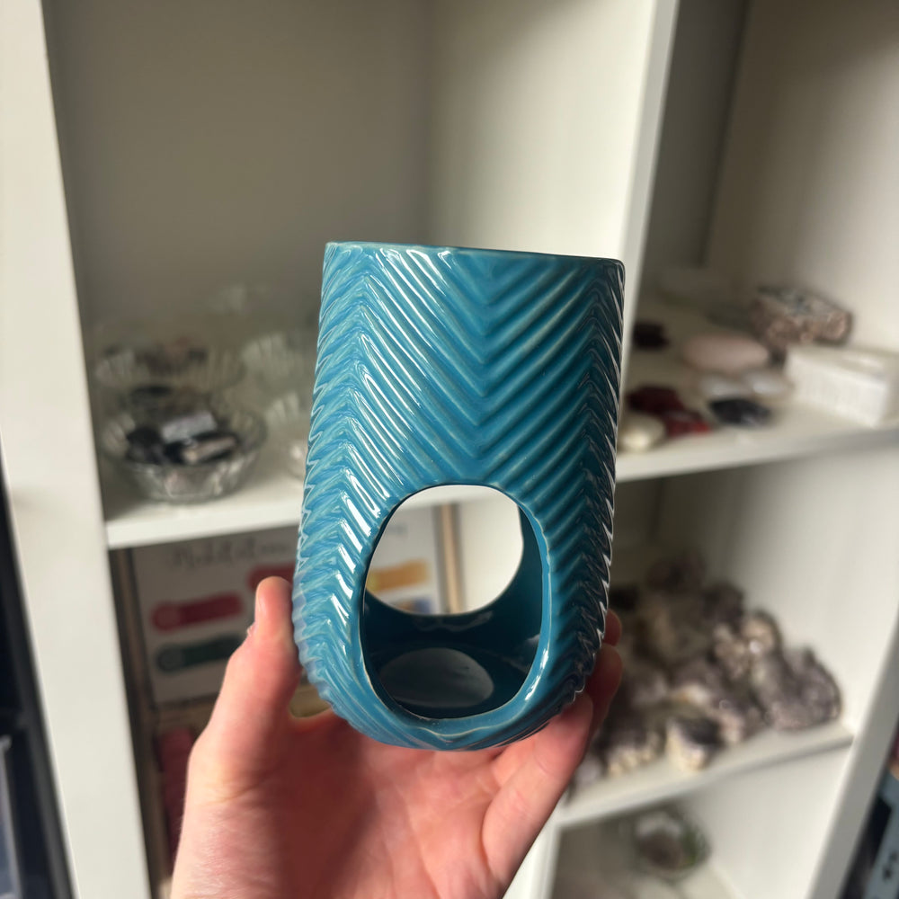 Turquoise Oil & Wax Melt Burner held in front of a shelf with various items.