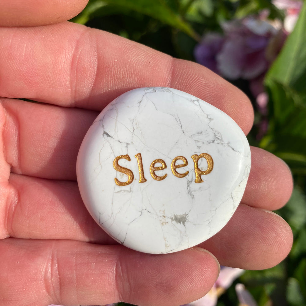 A white marble sleep stone with the word 'Sleep' in gold foil, held in a person's hand.