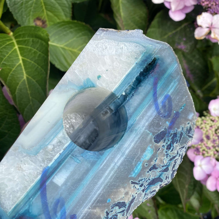 A hand cradling the agate crystal node block outdoors to display its flat sawn bottom base. The smooth base reveals a pre-drilled central socket designed to hold an LED light fitting, turning the specimen into a glowing sanctuary lamp.