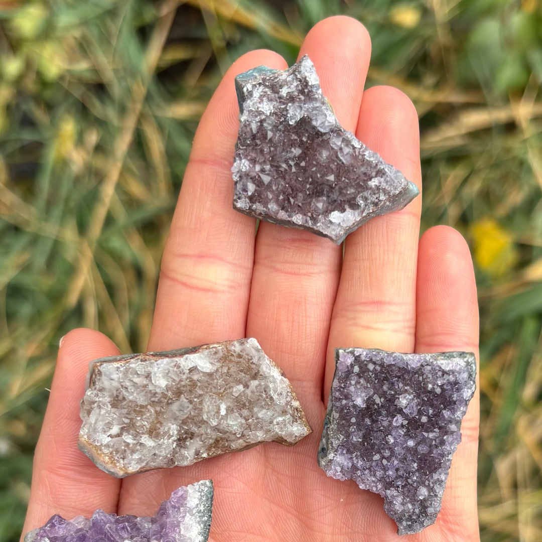 A hand presenting a trio of deep purple amethyst crystal fridge magnets, emphasizing their pocket-sized functional design.