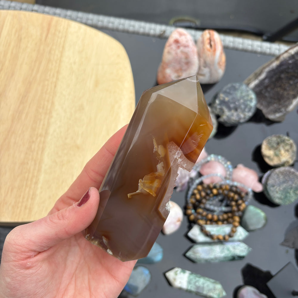 A hand holding the polished Agate generator point upright, highlighting the complex internal banding layers and the jagged opening of its glittering crystalline core under daylight.