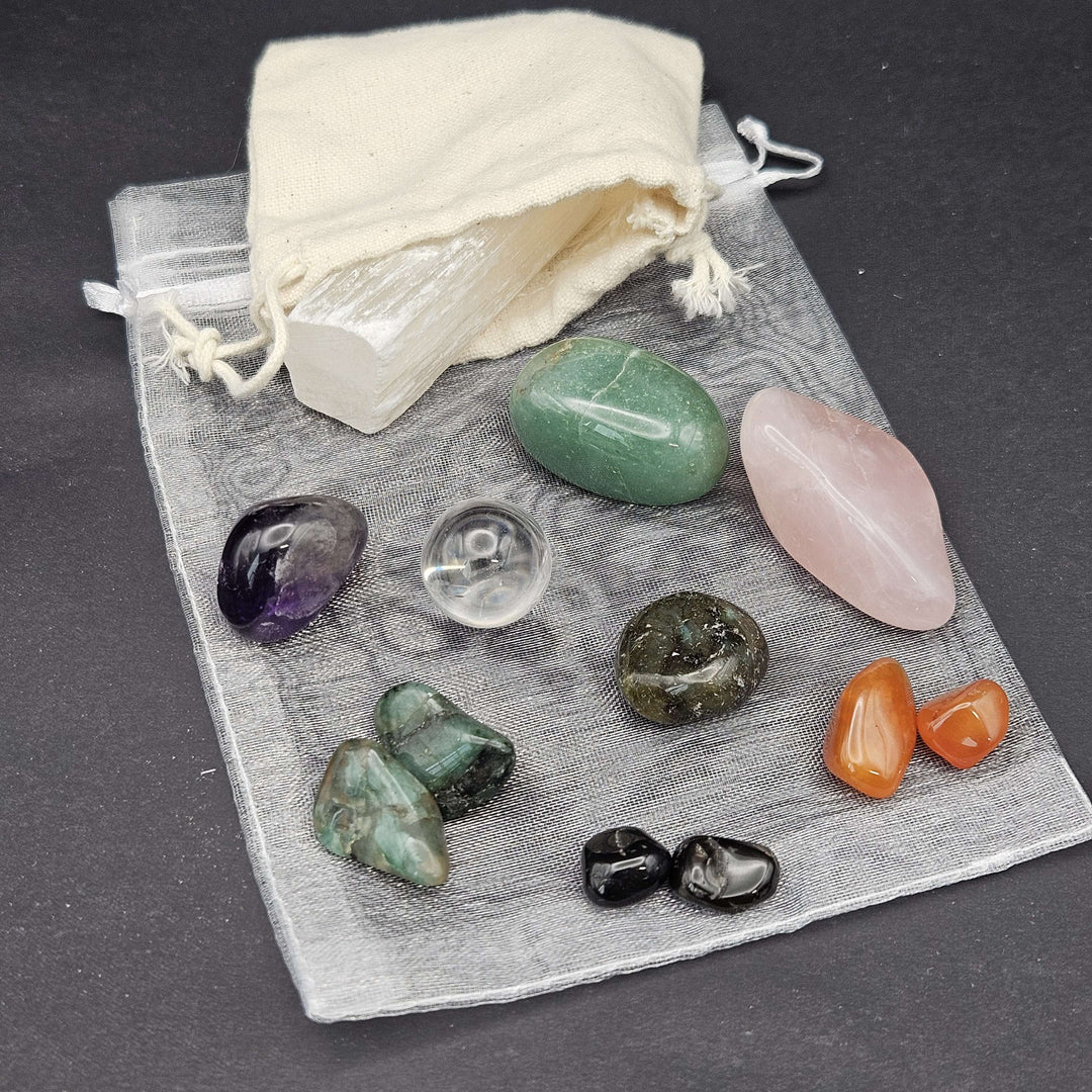 A collection of eleven beginner-friendly tumbled crystals laid out carefully over a sheer grey organza drawstring bag. A cream storage pouch sits in the upper corner against a dark background, highlighting an affordable everyday lifestyle setup.
