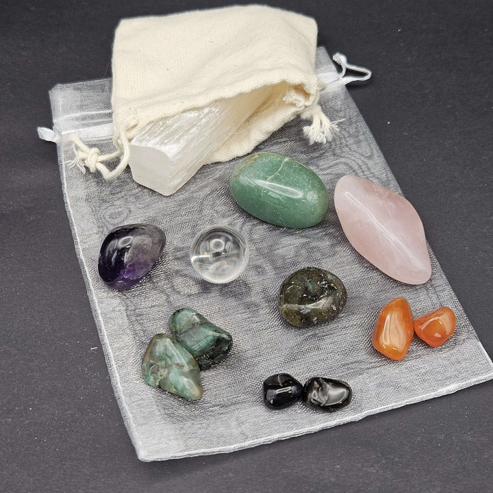 A collection of eleven beginner-friendly tumbled crystals laid out carefully over a sheer grey organza drawstring bag. A cream storage pouch sits in the upper corner against a dark background, highlighting an affordable everyday lifestyle setup.
