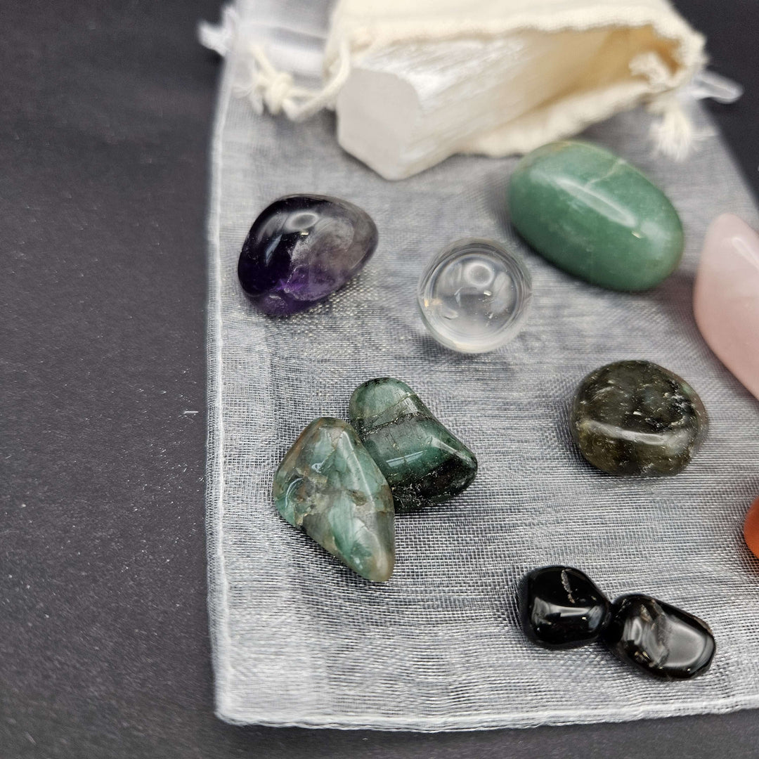 A collection of classic tumbled gemstones and a raw white selenite wand spread across a grey background. This accessible kit layout clearly displays how the pocket-sized stones fit seamlessly into a modern daily wellness routine. 