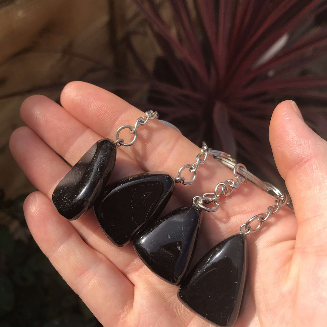 A hand presenting four glossy black onyx gemstone keychains to showcase their unique organic shapes and deep midnight hues.