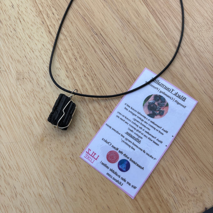 A flat lay view of the wire wrapped gemstone pendant resting on a wooden surface next to its printed crystal meaning card, detailing the traditional protection and grounding attributes that help dissolve chaotic thoughts.