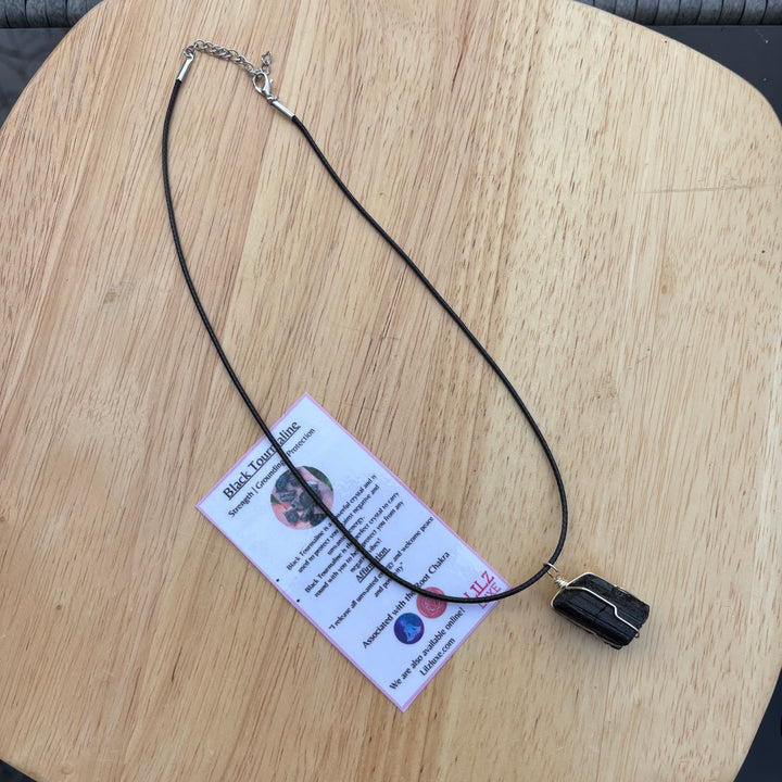 The raw stone protection pendant arranged vertically on a wooden table to display the full length of its comfortable 43cm black cord, proving how easily it loops over daily outfits to keep your energy centred.