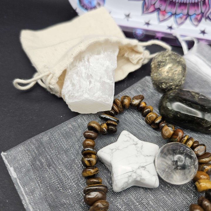 A close-up view focusing on a hand-carved white Howlite star stone resting atop a soft grey organza pouch. A brown and black tiger eye beaded bracelet wraps around the base, channelling inner strength, focus, and grounding properties. 