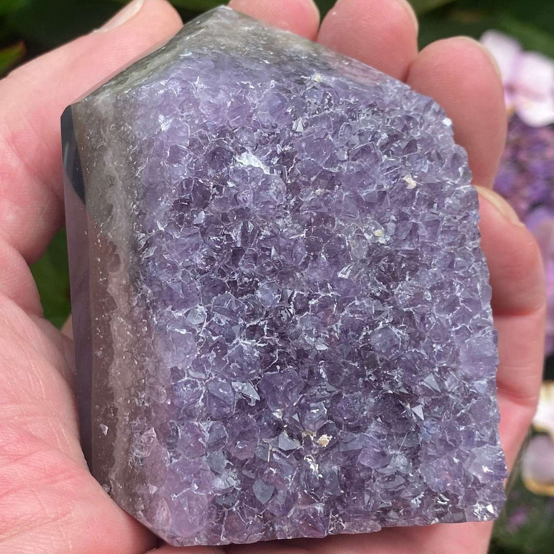 A macro close-up view of a substantial, chunky amethyst crystal generator point held upright in a hand. The unique statement piece features a glittering face of raw purple amethyst druzy crystals combined with polished, six-sided column facets near the top termination apex.
