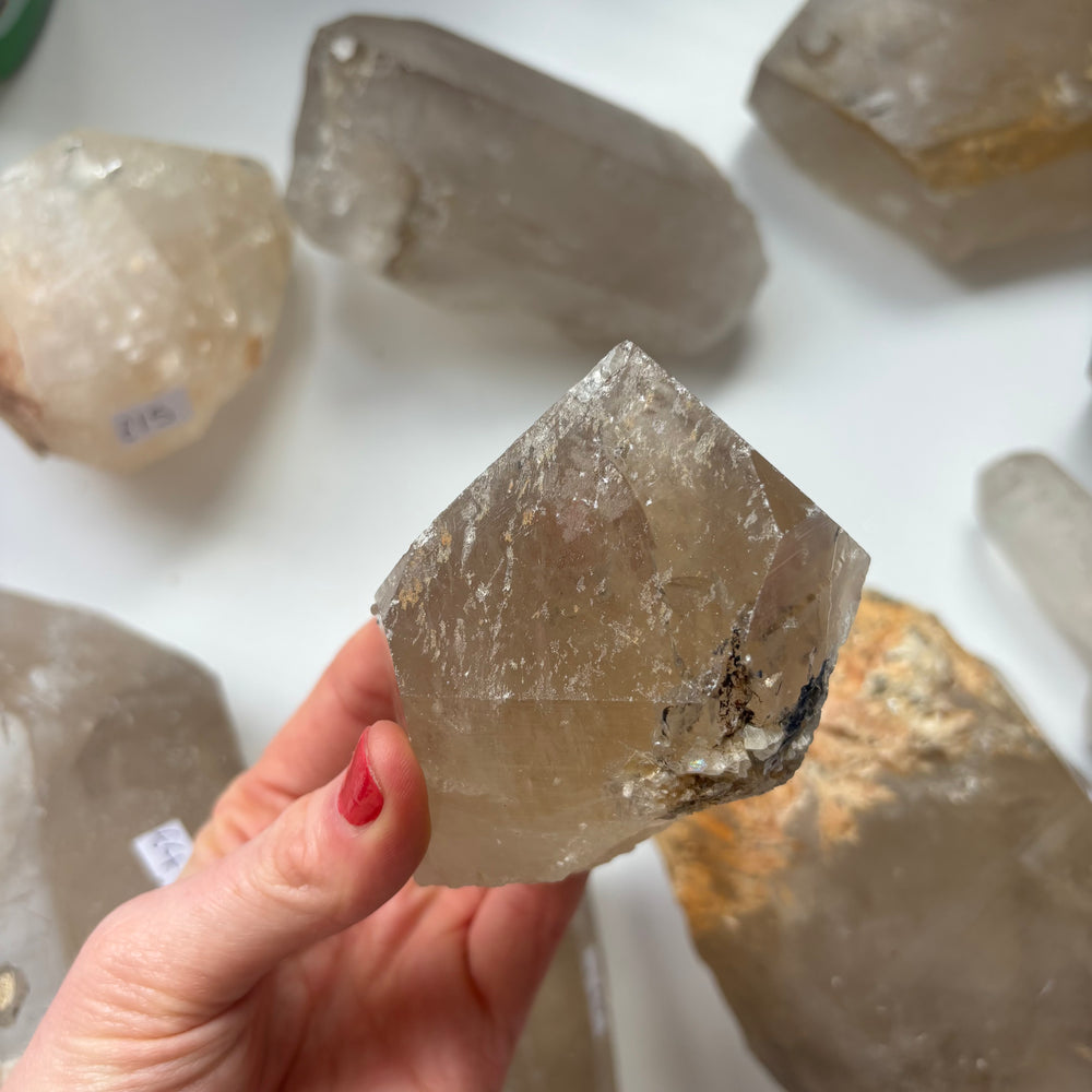 A close-up view of a hand holding a chunky rough clear quartz stone at a low angle, showcasing the icy unpolished textures and authentic earth-born birthmarks that help sweep away mental static and restore fresh motivation.
