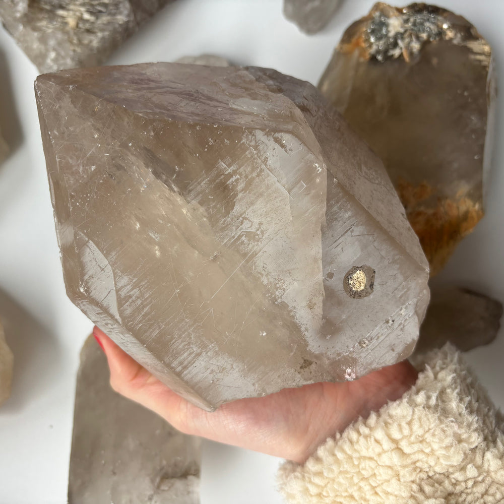 A two-handed cradle showcasing the substantial size and heavy weight of a colossal unpolished clear quartz crystal cluster highlighting frosted natural surfaces.
