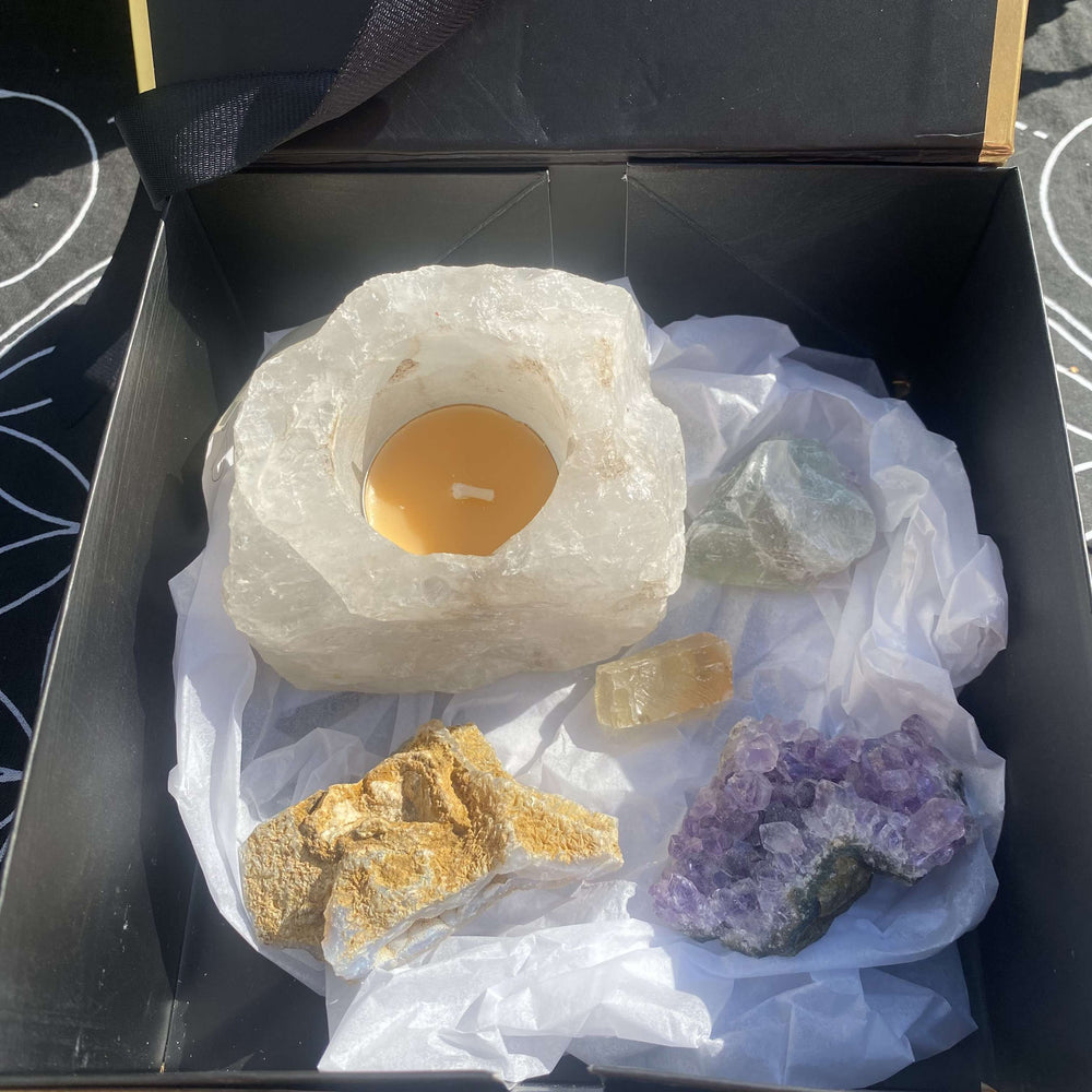 An overhead view looking into a premium, square open gold gift box. The five healing crystal specimens are nestled safely together on top of a soft bed of protective white tissue paper packaging, presenting a luxury unboxing experience for crystal lovers.