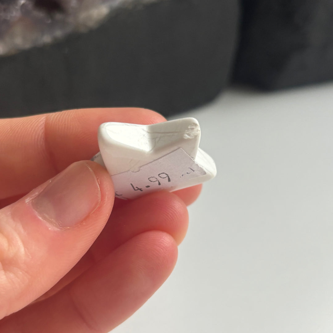 Fingers holding the side profile edge of the discounted white howlite star carving close up, clearly showing a slight natural chip on one of its celestial points to highlight the authentic character of this Quirky Corner clearance item.