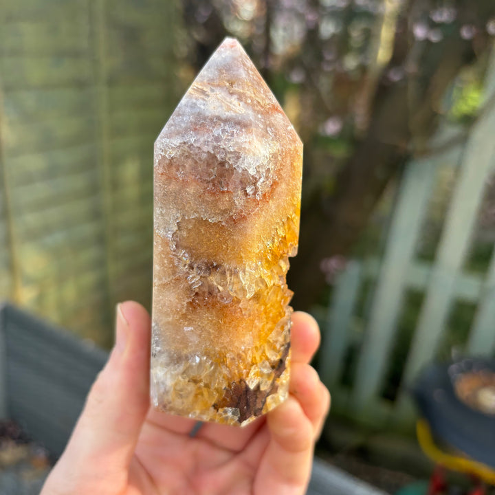 A hand holding the upper section of the discounted pink amethyst crystal tower close up, revealing a small physical chip right on its pointed tip to illustrate the unique story of this clearance collection item.