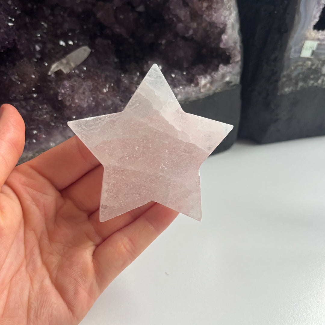 A hand presenting the discounted selenite pocket star talisman flat in the palm, highlighting the vertical satin grains and unique natural surface marks of this budget-friendly clearance crystal.