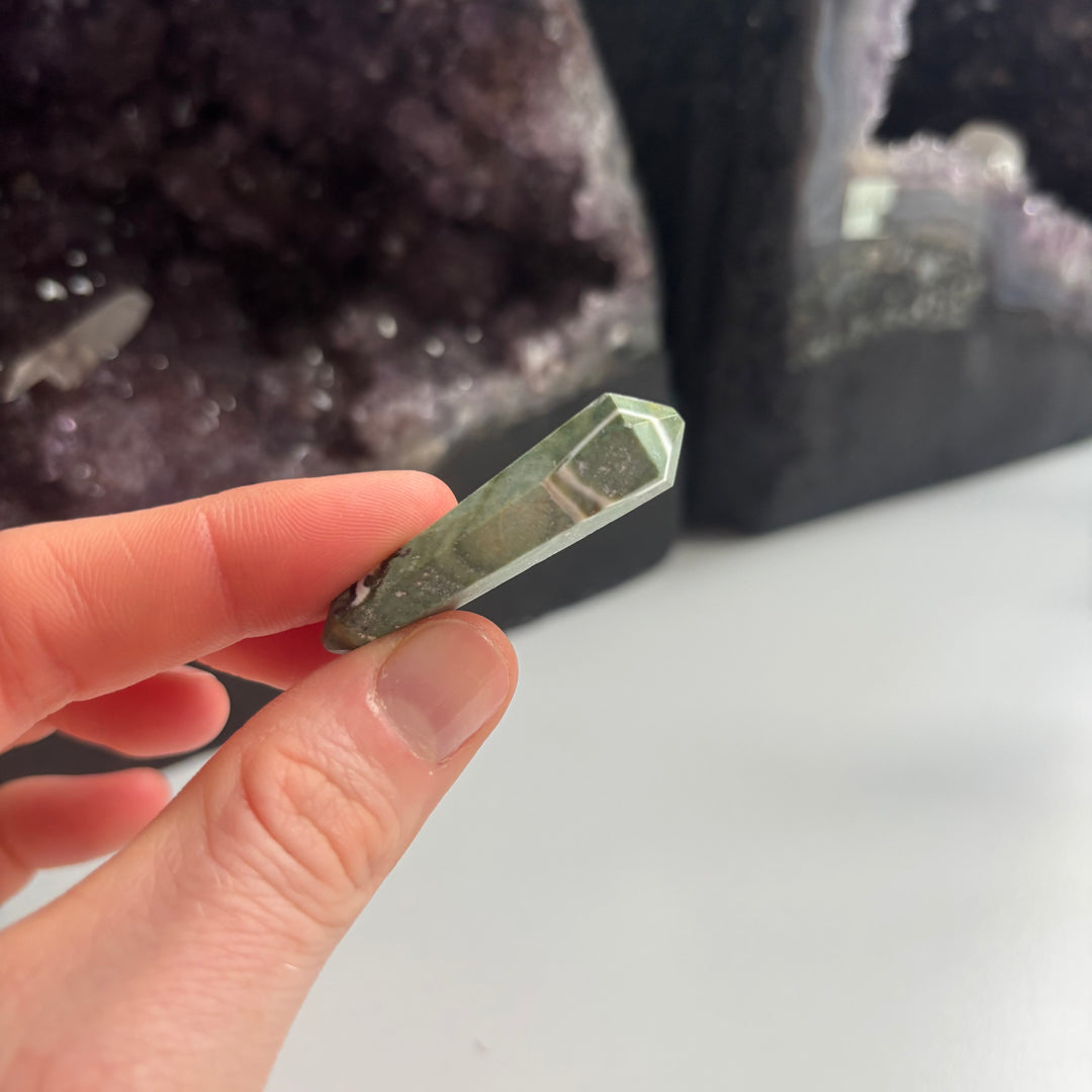 Fingers holding the faceted edge of the discounted serpentine terminated point close up, revealing a small natural chip on one of its tips to showcase the authentic character of this Quirky Corner clearance item.
