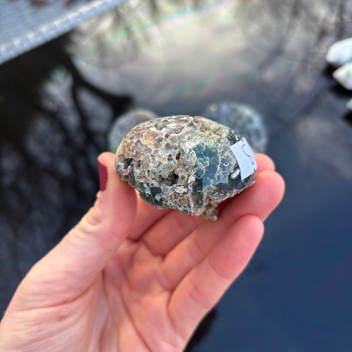 A top-down view of a hand presenting a grape agate crystal sphere, highlighting its natural mineral clusters and earthly imperfections.