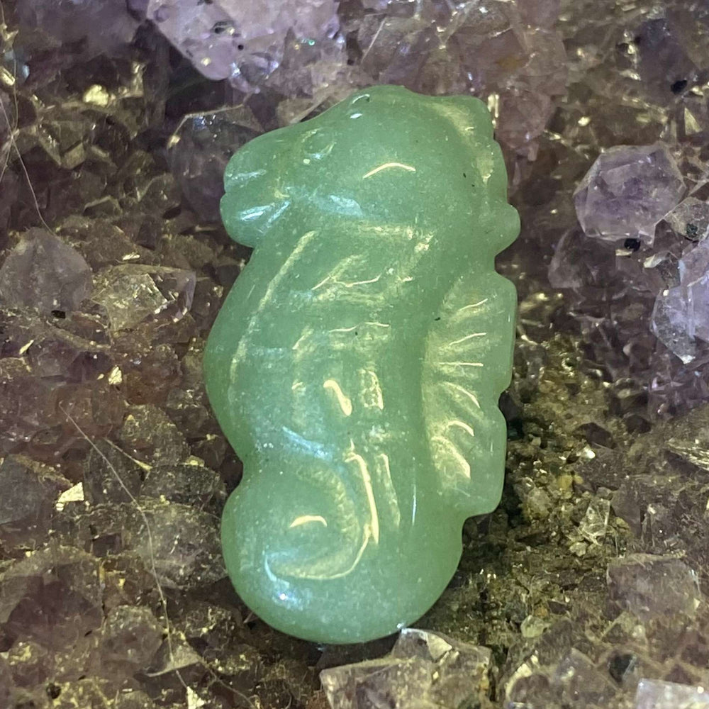 A slightly distant shot showcasing the full profile of the green aventurine seahorse carving. The mint-green crystal structure gleams softly against the raw, texturised violet amethyst background, emphasizing its gentle ocean energy and premium artisan details for a crystal collection.