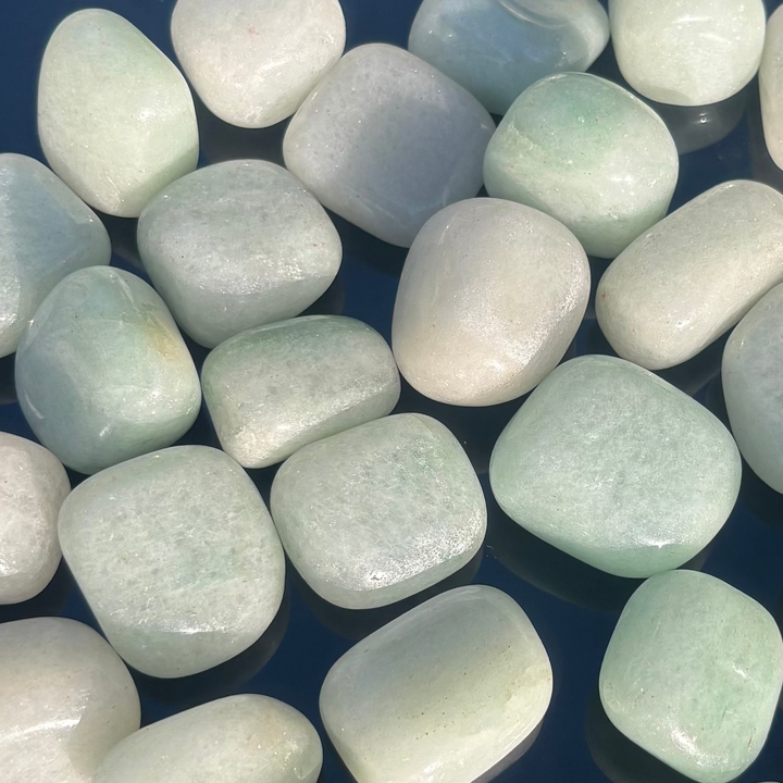 A crisp close-up view of a pile of smooth green aventurine pocket stones, detailing the natural internal fractures, rounded organic contours, and cool glassy finishes that help welcome fresh beginnings.