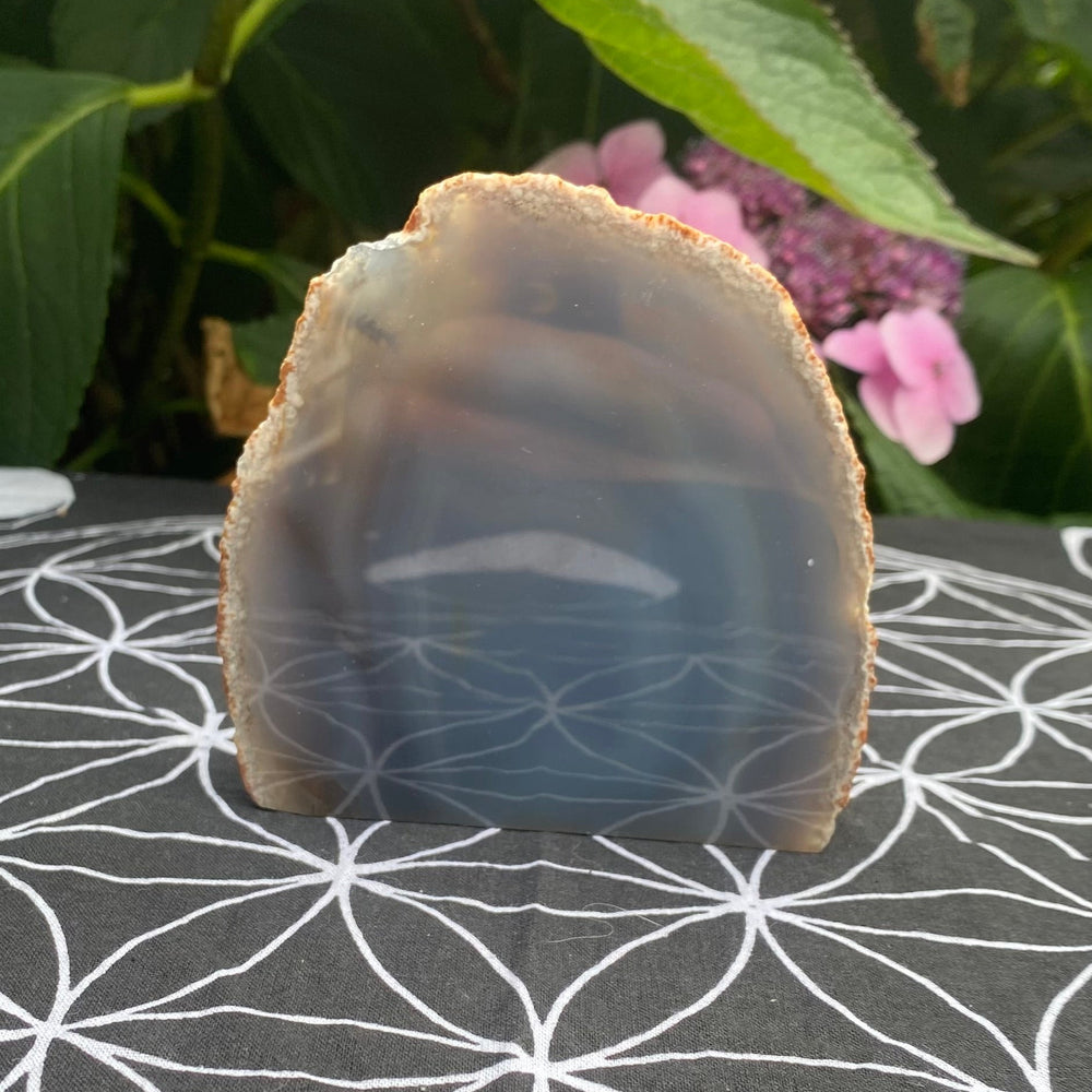 Natural grey agate slice standing upright on a black and white sacred geometry Flower of Life grid mat.
