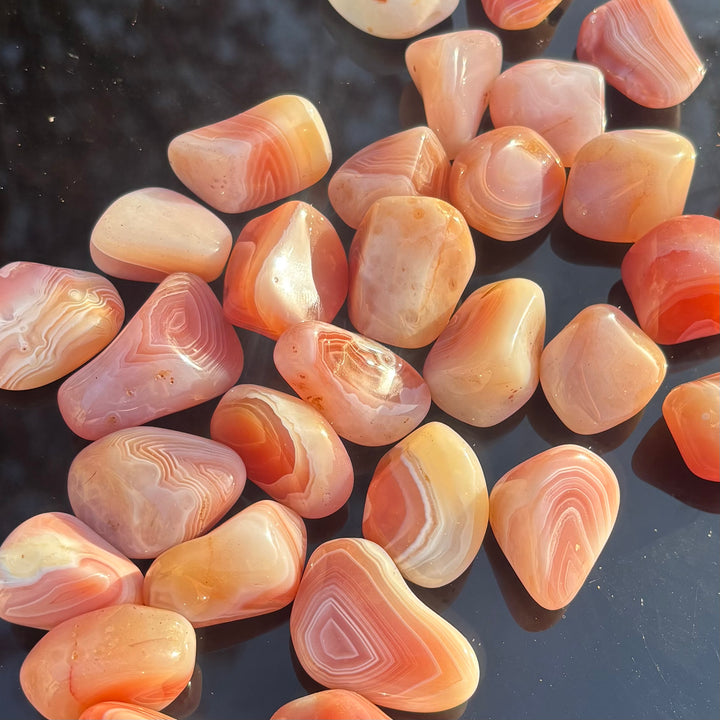 A collection of glossy Apricot Agate tumble stones scattered across a reflective black table outdoors, ideal for heart and solar plexus chakra focus or emotional healing rituals.