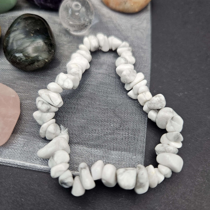 A close-up view focusing entirely on the white Howlite chip stretch bracelet arranged in a neat circular shape on a dark surface. The unique grey webbing patterns of the silky stones highlight a comforting texture for casual wear. 