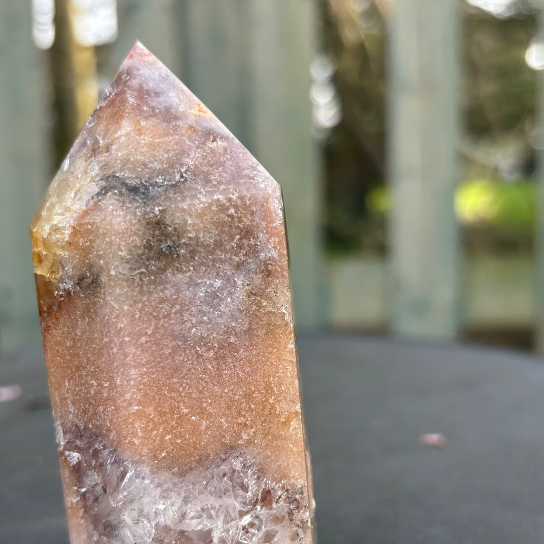 A close-up shot of the lower column and flat cut base of the imperfect pink amethyst obelisk tower held in a hand, displaying the solid structure and unique landscape markings left by the Earth.