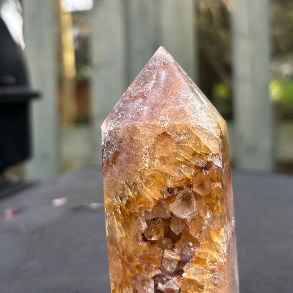 A close-up outdoor view of the imperfect pink amethyst crystal tower tip, highlighting the unique raw textures, internal veiling, and natural mineral patterning along its faceted crystal point.
