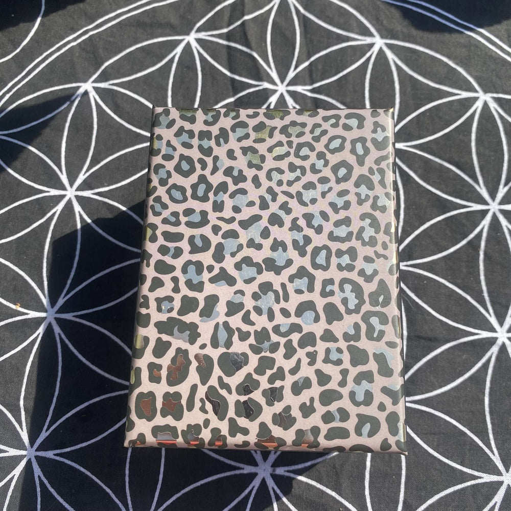 A top-down view of the closed rectangular crystal gift box resting flat on a black and white Flower of Life grid mat outdoors. The decorative lid features a striking brown and black leopard print pattern, highlighting a stylish and ready-to-wrap presentation.