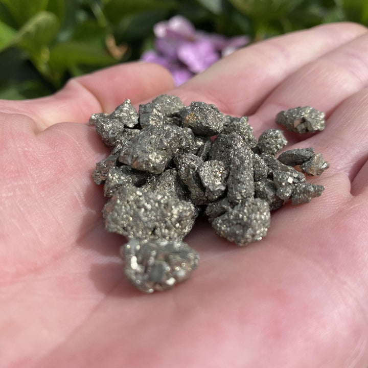 A macro close-up view of small unpolished pyrite cluster pieces held in a hand, capturing the sharp metallic facets and organic stone ridges perfect for crystal grids.

