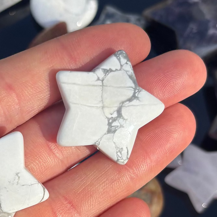 A hand tilting a miniature polished howlite star token to reveal its smooth glossy curves and unique organic grey shading, perfect for slipping inside a coat pocket or displaying on a bedside table to encourage sweet, comforting slumber.