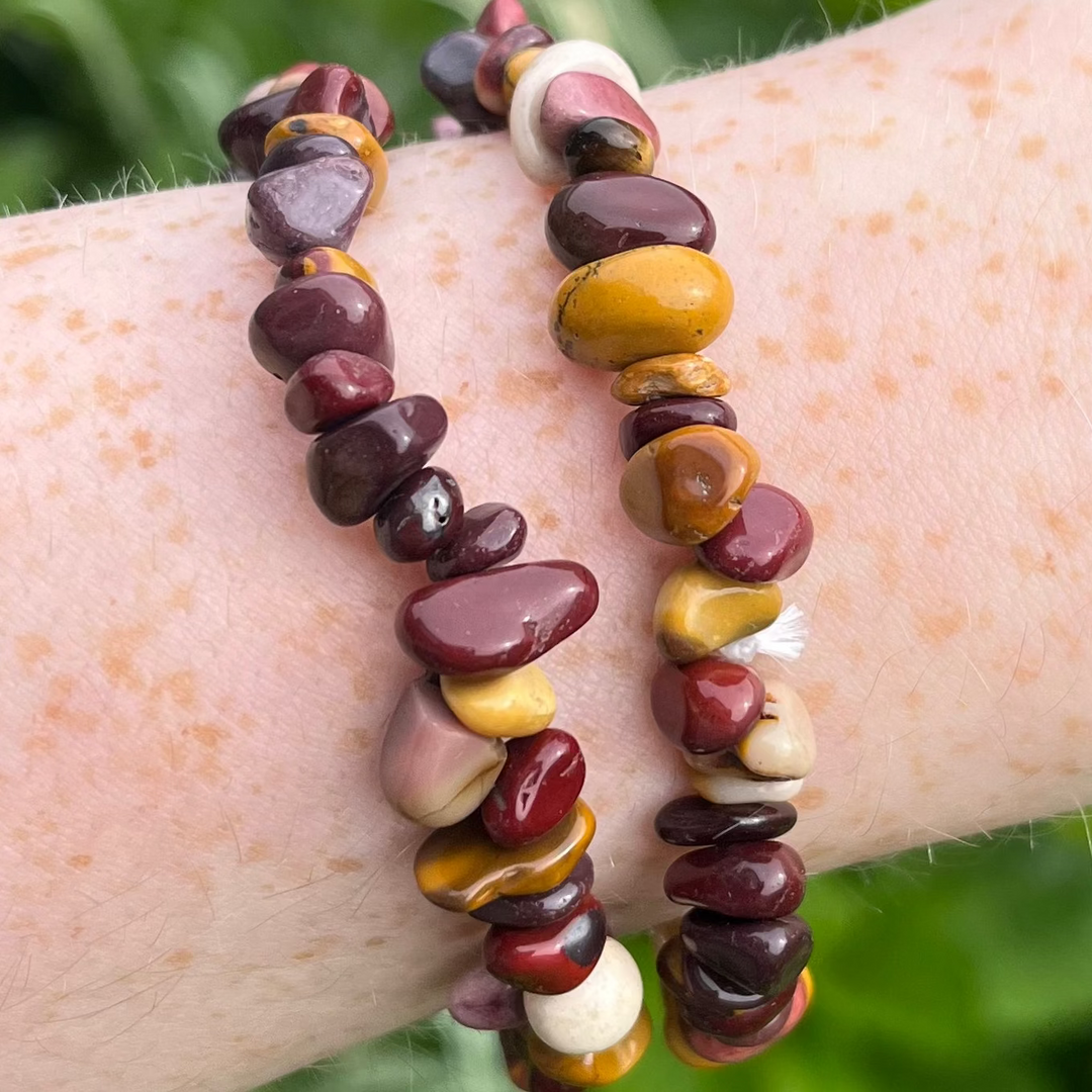 A close-up view of two Mookaite crystal chip bracelets worn stacked on a wrist. The polished natural gemstone pieces feature an organic, texturised look, showing off a gorgeous autumnal mix of rich burgundies, mustard yellows, and creamy tones.