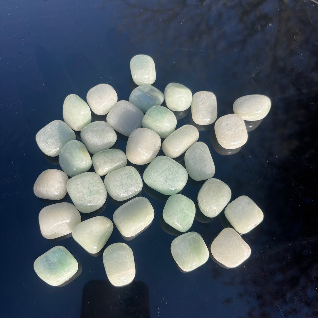 A top-down view of a scattered pile of natural green aventurine tumbled gemstones resting against a dark background, illustrating an ideal aesthetic for pocket companions, desk displays, or a supportive gift.