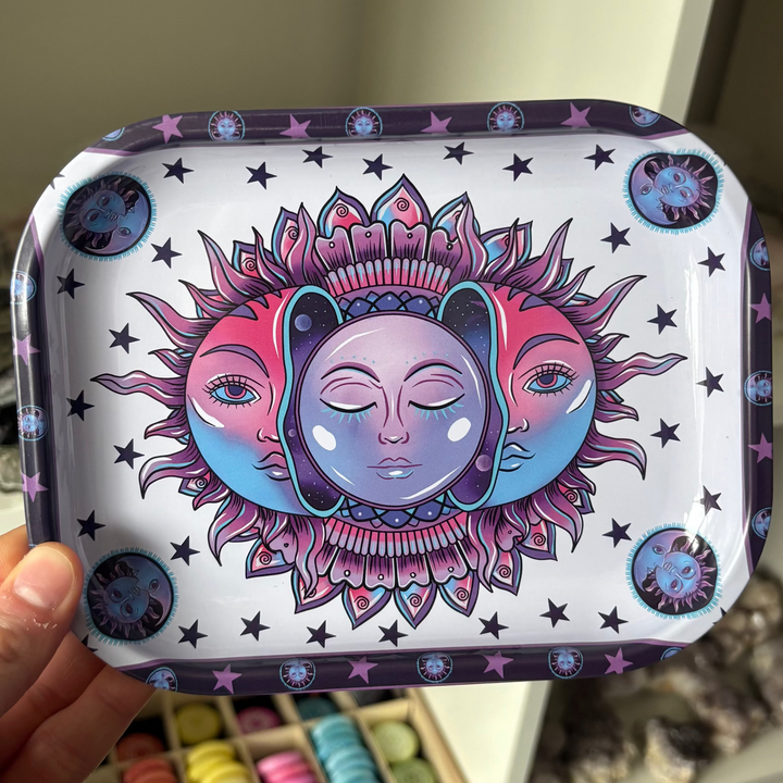 A hand holding a rectangular display tray featuring a vibrant pink, purple, and blue celestial sun and moon design with third eye motifs.