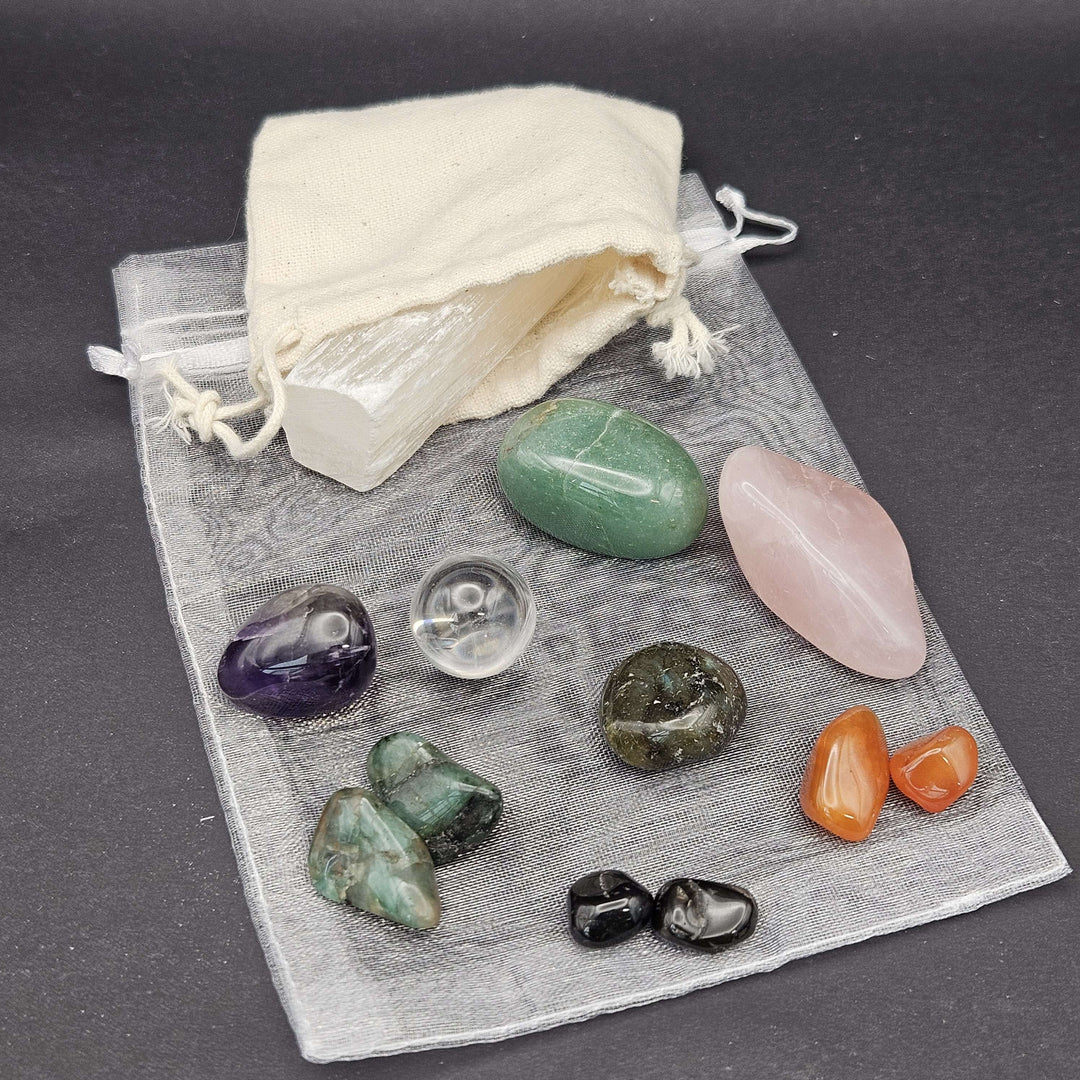 An overhead view showcasing a pocket crystal starter kit arranged neatly on a dark charcoal surface. The setup displays mini tumbled gemstones alongside soft fabric and mesh storage bags, designed to invite a touch of everyday magic.