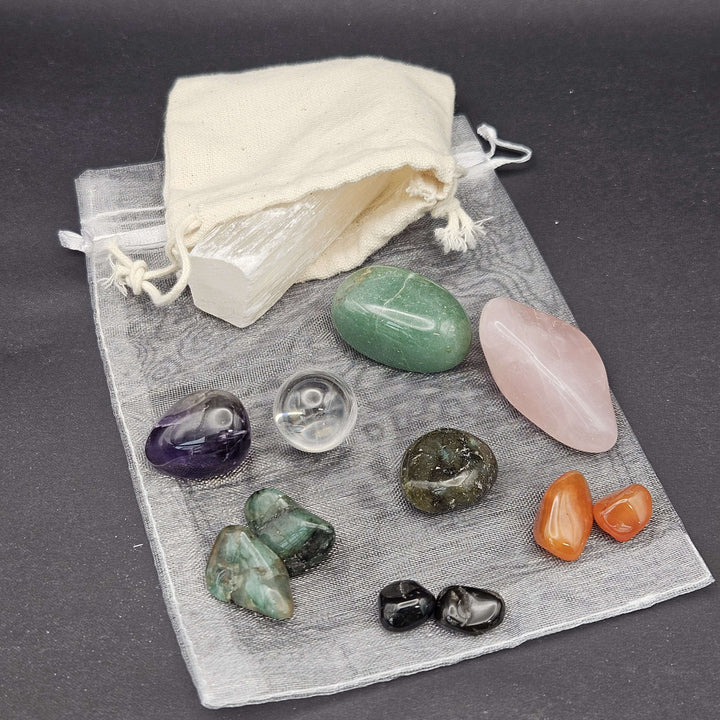 An overhead view showcasing a pocket crystal starter kit arranged neatly on a dark charcoal surface. The setup displays mini tumbled gemstones alongside soft fabric and mesh storage bags, designed to invite a touch of everyday magic.