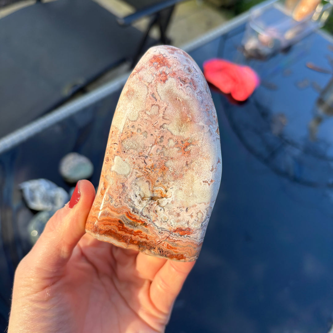A hand rotating the polished pink and apricot Agate freeform block, displaying the complex natural ribbon patterns and earthborn features wrapping across the curved stone.