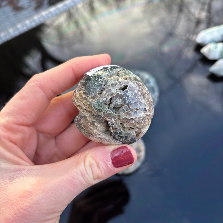 A hand holding a unique polished purple Grape Agate crystal freeform stone to emphasize its comfortable, pocket-sized organic shape.