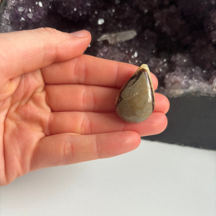 A hand presenting the side profile of a polished septarian jasper pocket talisman from the clearance collection, detailing its smooth rounded edges and ancient geological layers designed to bring emotional safety and grounding comfort.