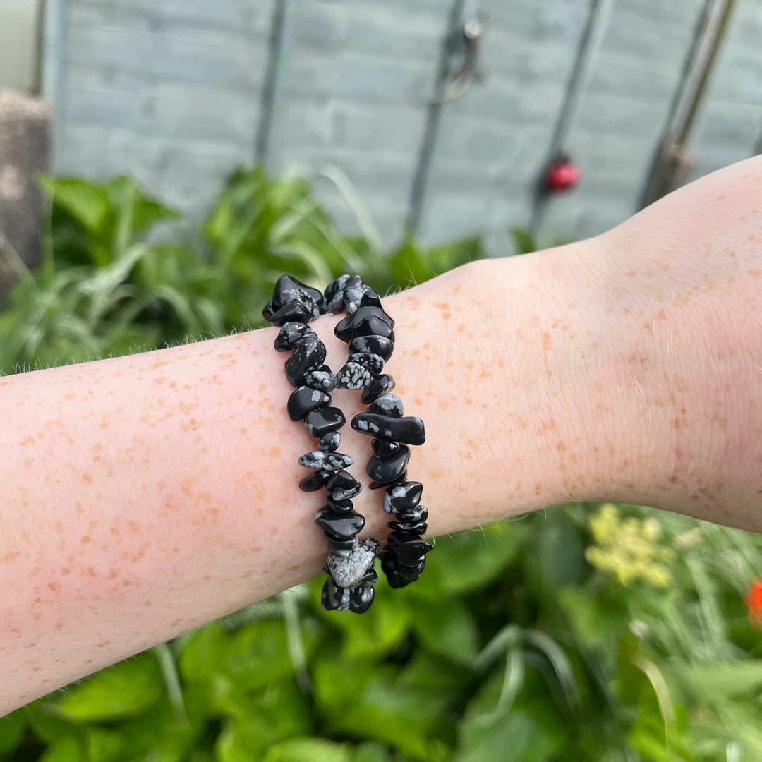 A person showcasing a lightweight, flexible black and white snowflake obsidian stretchy chip bracelet on their wrist outside, highlighting the comfortable everyday jewellery styling scale and smooth tumbled textures under daylight.