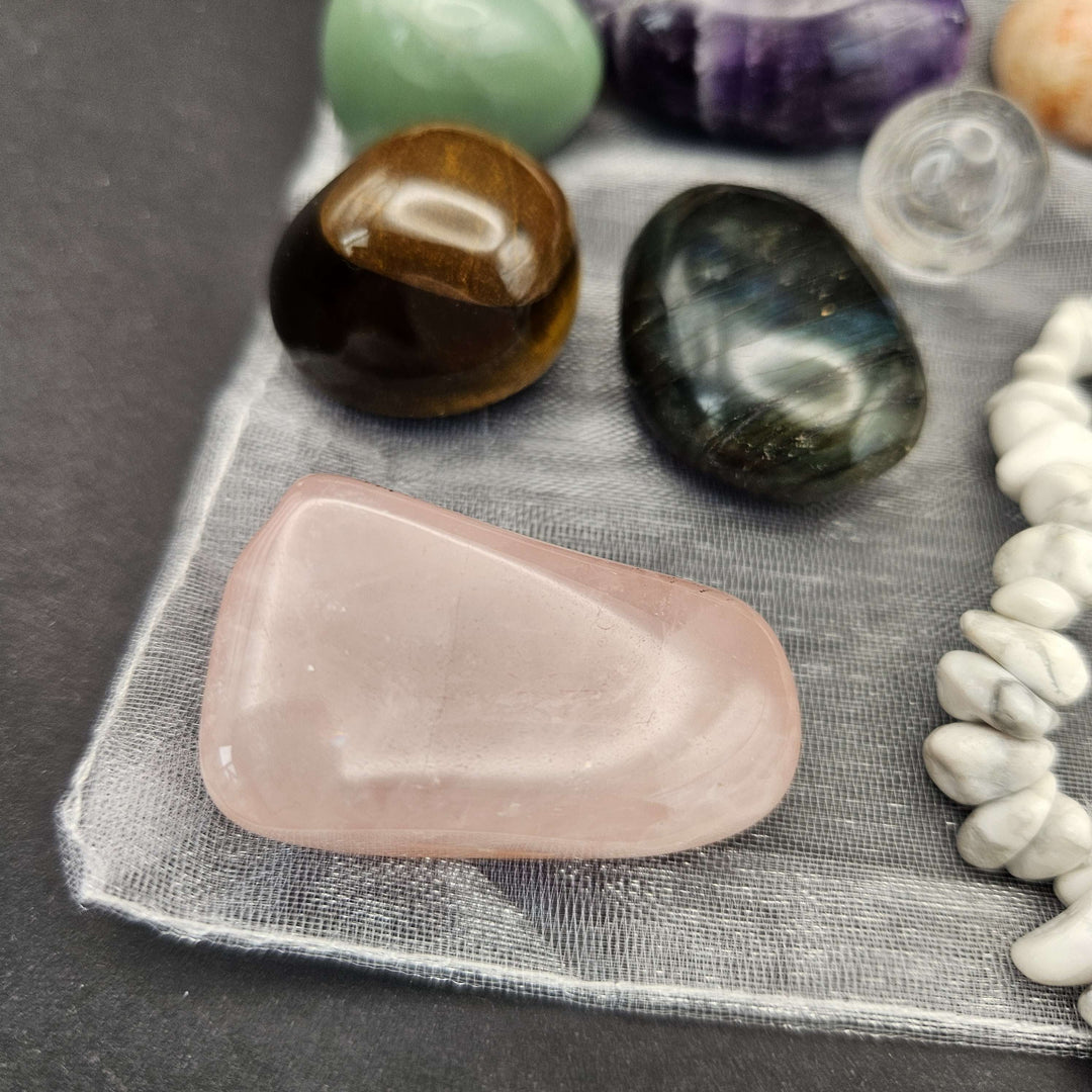 A detailed macro perspective looking at polished tumble stones including a large flat rose quartz, tiger eye, and emerald. The glossy faces catch ambient light beautifully, showcasing the authentic geological birthmarks from the Earth.  