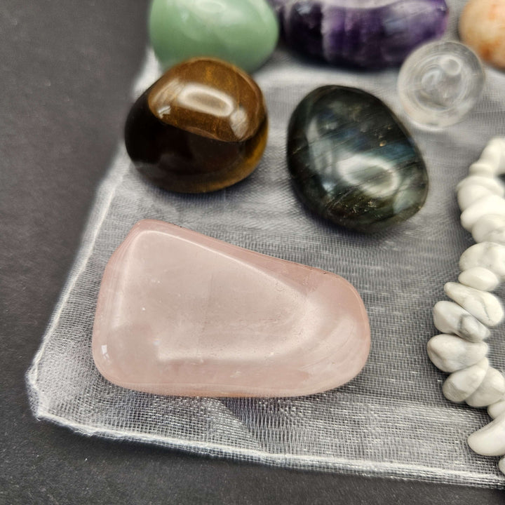 A detailed macro perspective looking at polished tumble stones including a large flat rose quartz, tiger eye, and emerald. The glossy faces catch ambient light beautifully, showcasing the authentic geological birthmarks from the Earth.  