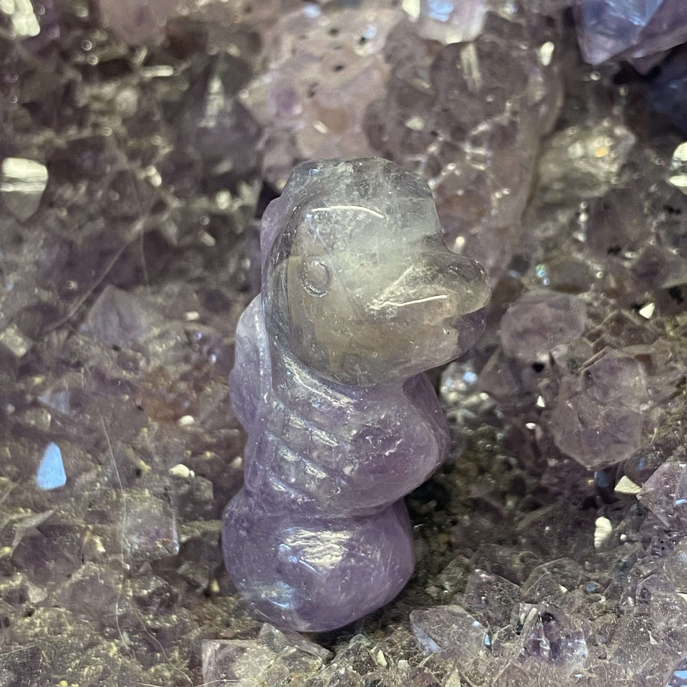 An elevated side-angle view of a translucent amethyst gemstone seahorse figurine showing internal frost lines resting on a bed of dark mineral fragments.
