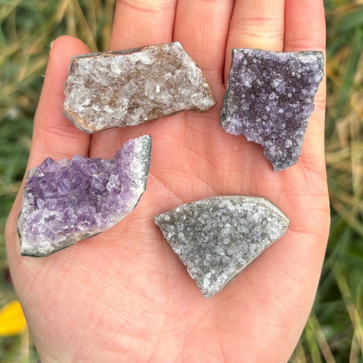 A close-up view of four raw purple amethyst geode slice magnets held in a palm to showcase their distinctive mineral shapes.