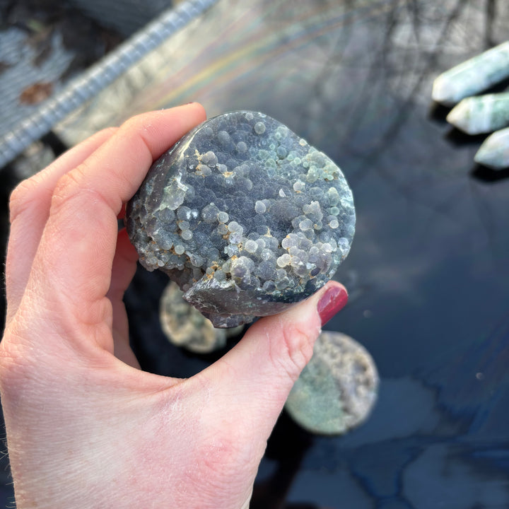 A person holding a textured Grape Agate freeform stone in their palm, highlighting the natural chalcedony clusters and earthy indents.