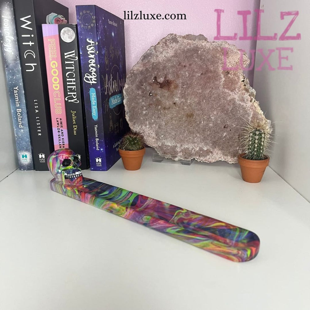 A high-angle view showing the twenty-four-centimetre resin incense ashcatcher arranged on a shelf. Styled next to books and a large amethyst cluster geode, this layout highlights how the smooth marbling effect brings a colourful energy to your room.