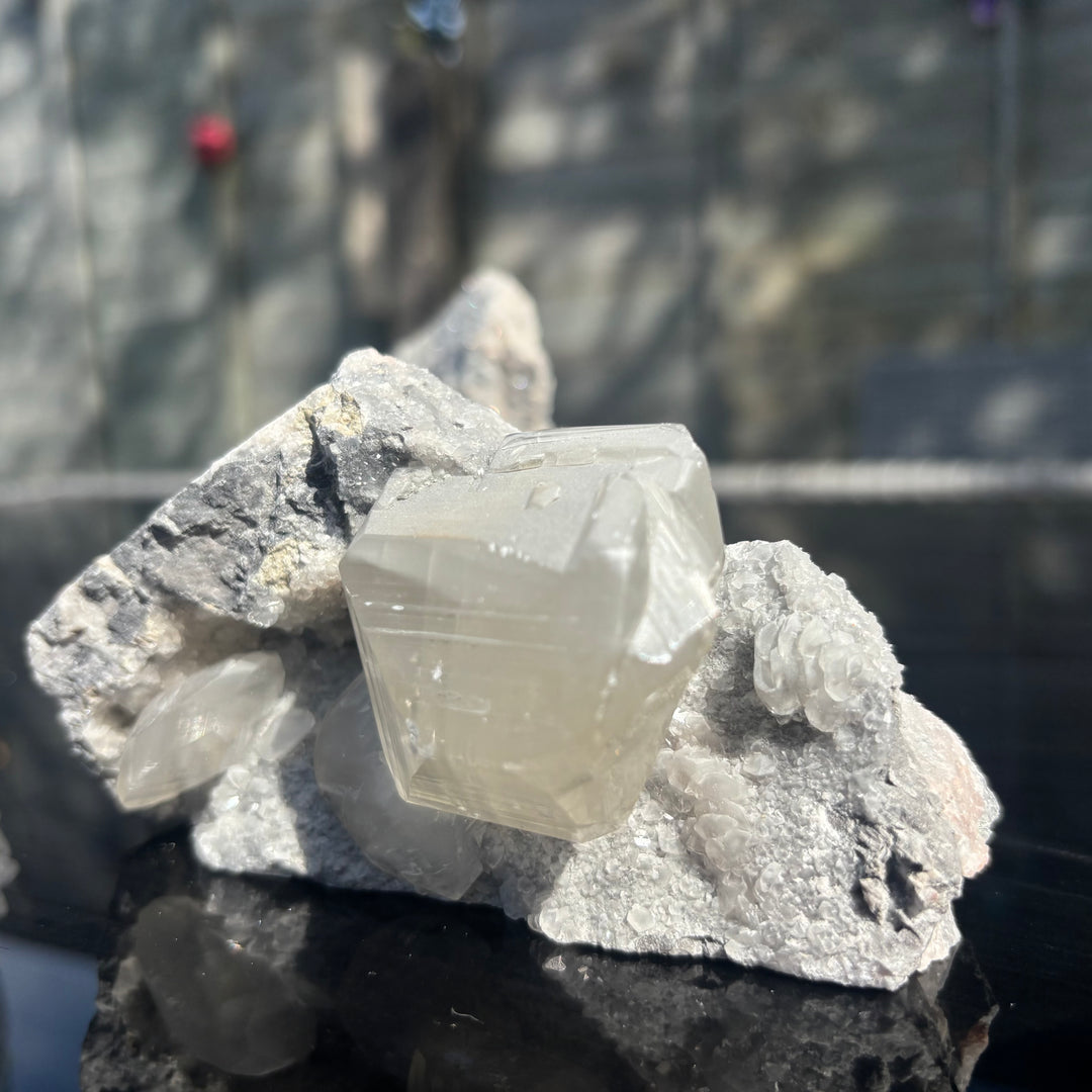 A low-angle shot of the raw grey chalcedony cluster standing unsupported on a glossy surface outdoors, detailing the sharp, crisp calcite cubes resting in a shimmering matrix pocket to create a balanced aura for mindful reflection.