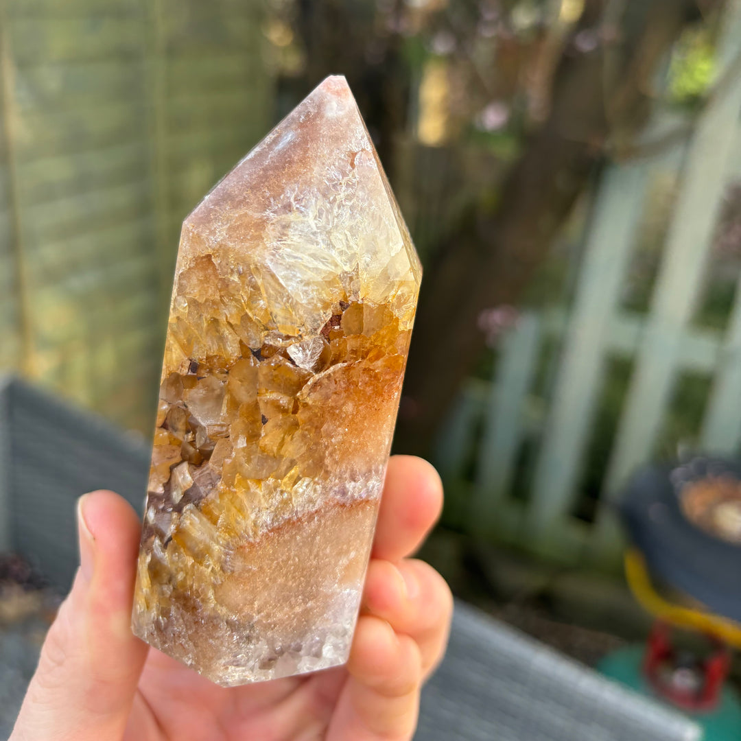 A hand presenting a side profile view of the raw geological pink amethyst tower facets, capturing how the natural light illuminates its intricate earthy growth patterns to invite soft inner trust.