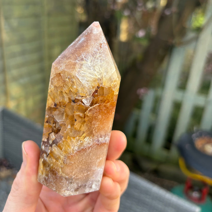 A hand presenting a side profile view of the raw geological pink amethyst tower facets, capturing how the natural light illuminates its intricate earthy growth patterns to invite soft inner trust.